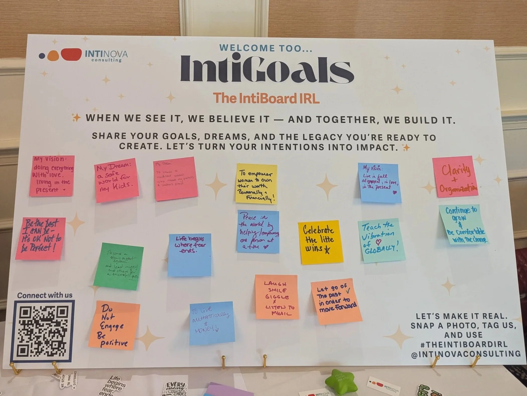 A large white board with numerous colorful sticky notes containing personal goals and visions, framed by gold clips at the bottom, and a QR code in the bottom left corner.