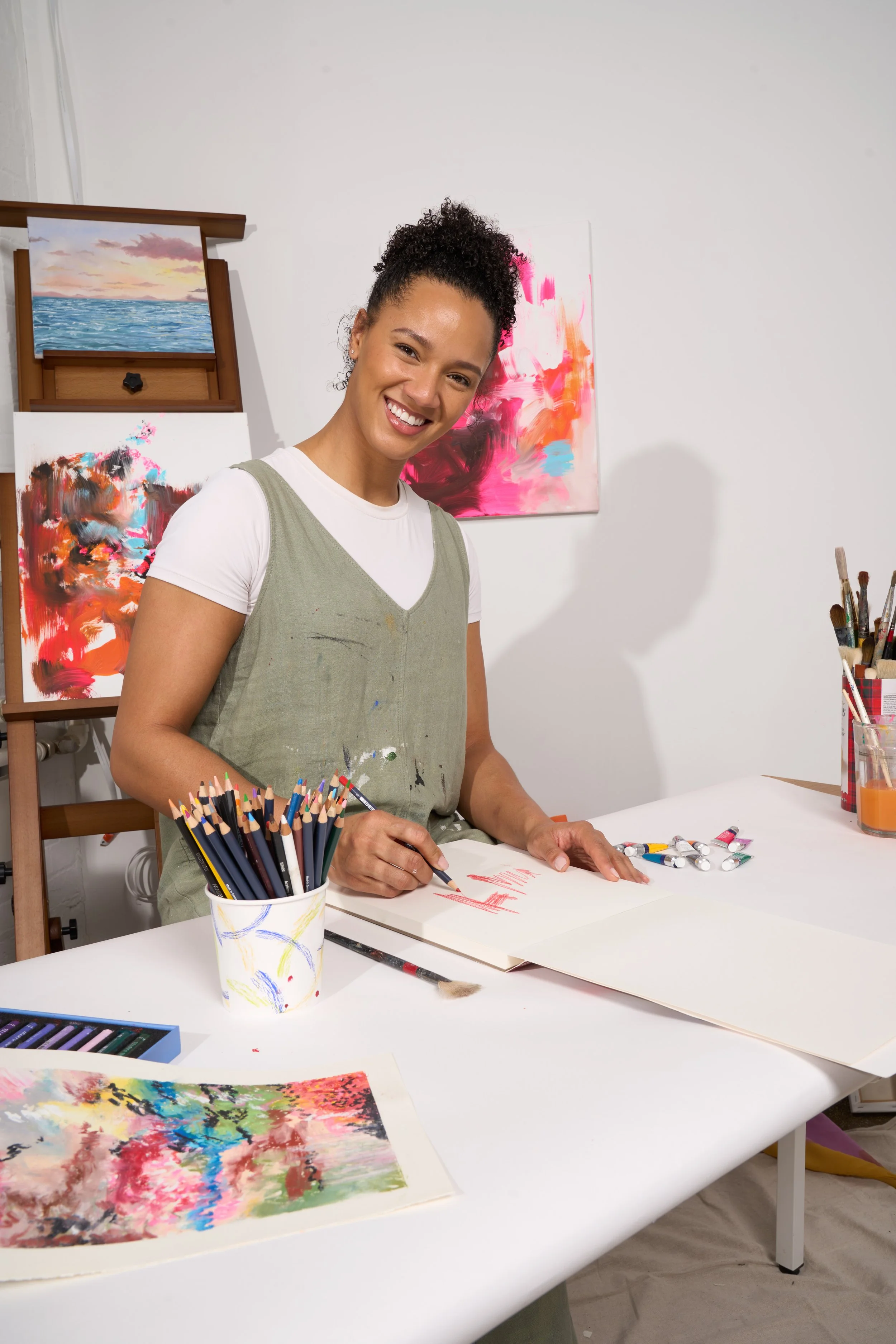 Artist Demi Dawkins smiling while creating colourful artwork at a table in her studio