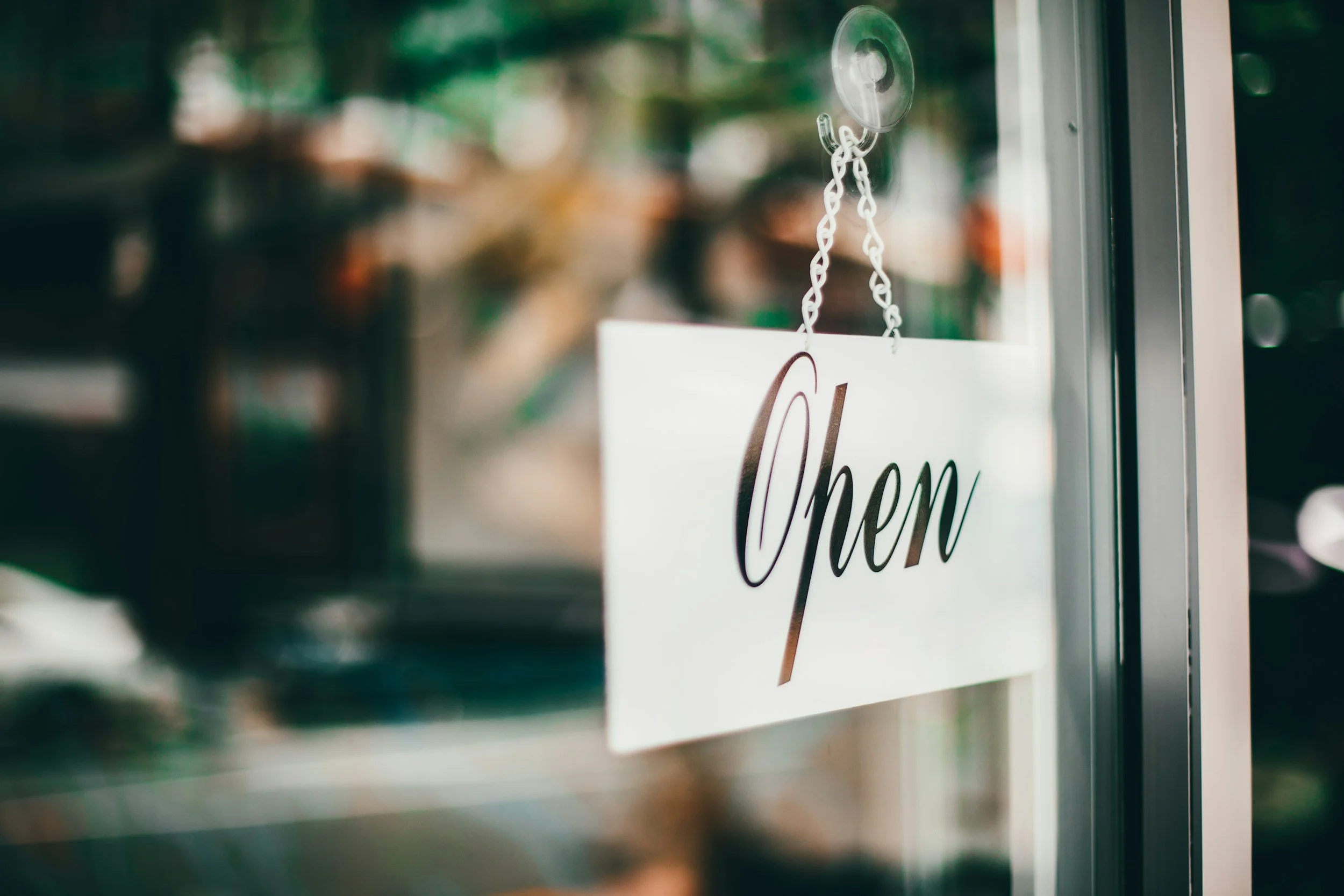 Close-up of a white 'Open' sign hanging on a glass door with a blurred background.
