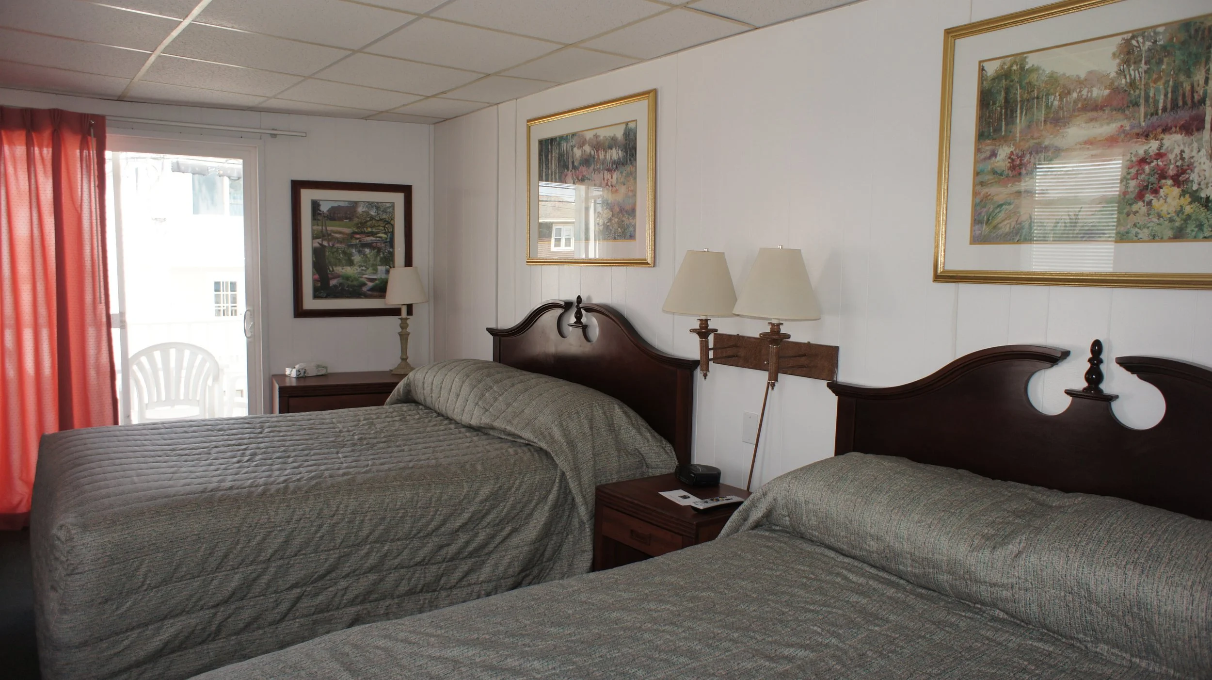 Modern wooden house with large glass window, surrounded by yellowish greenery, mountains in the background