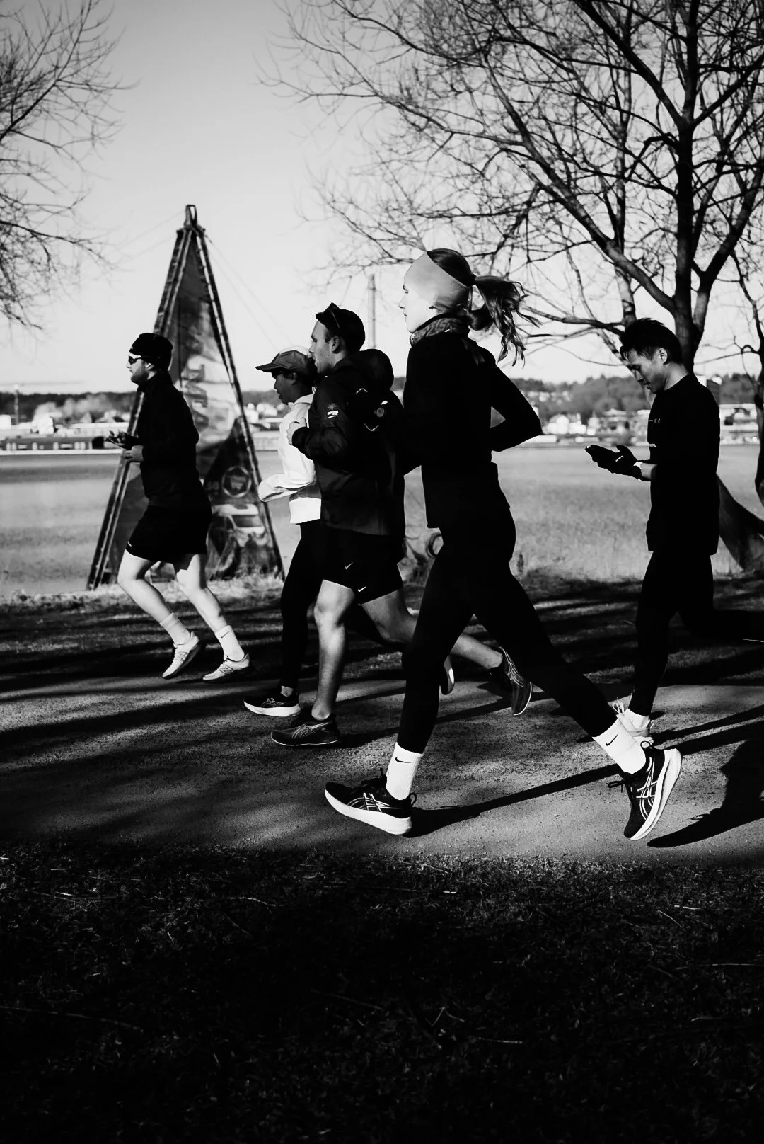 People jogging on a paved path beside leafless trees on a sunny day.
