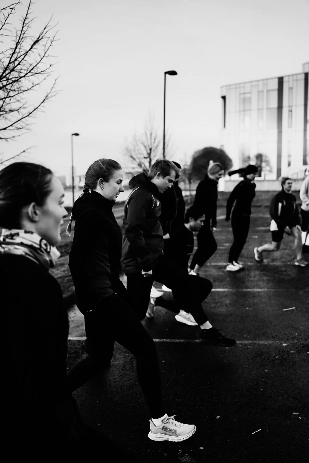 Group of people in athletic clothing preparing for a race outdoors, standing in a line, some stretching or warming up.