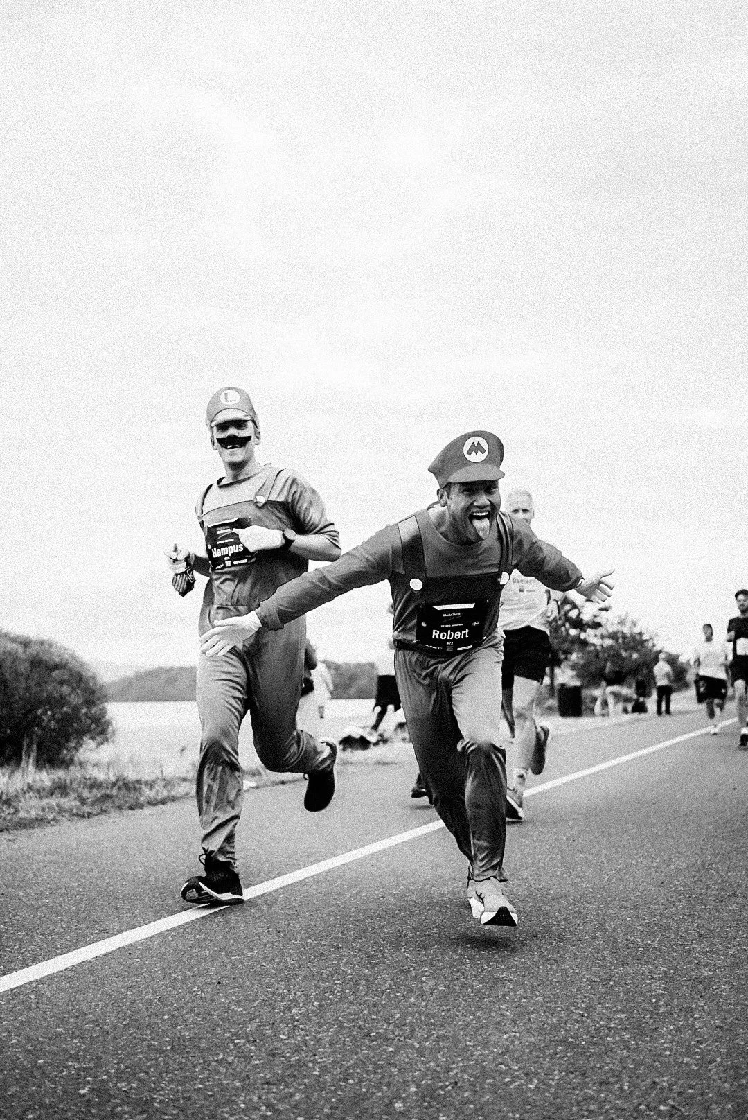 People dressed as Mario and Luigi running on a road during a marathon or race, with other runners in the background.