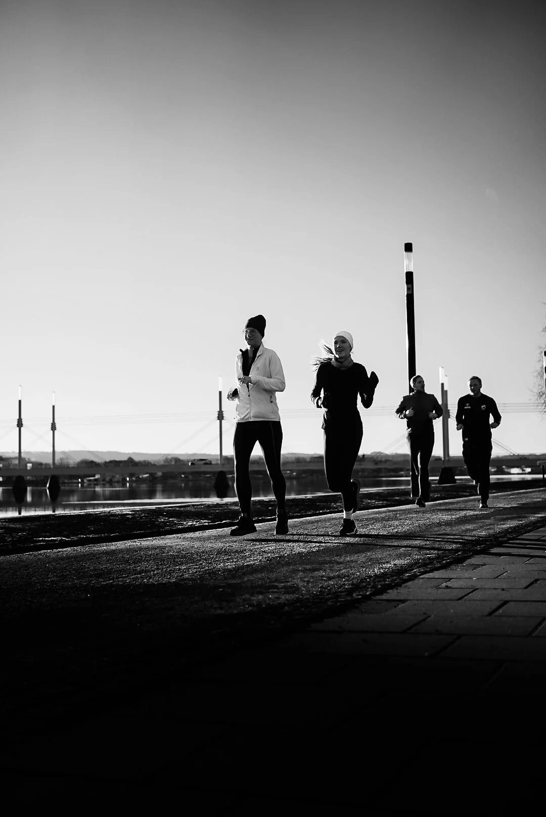 Four people jogging or running along a pathway during early morning or late evening, with a clear sky in the background.