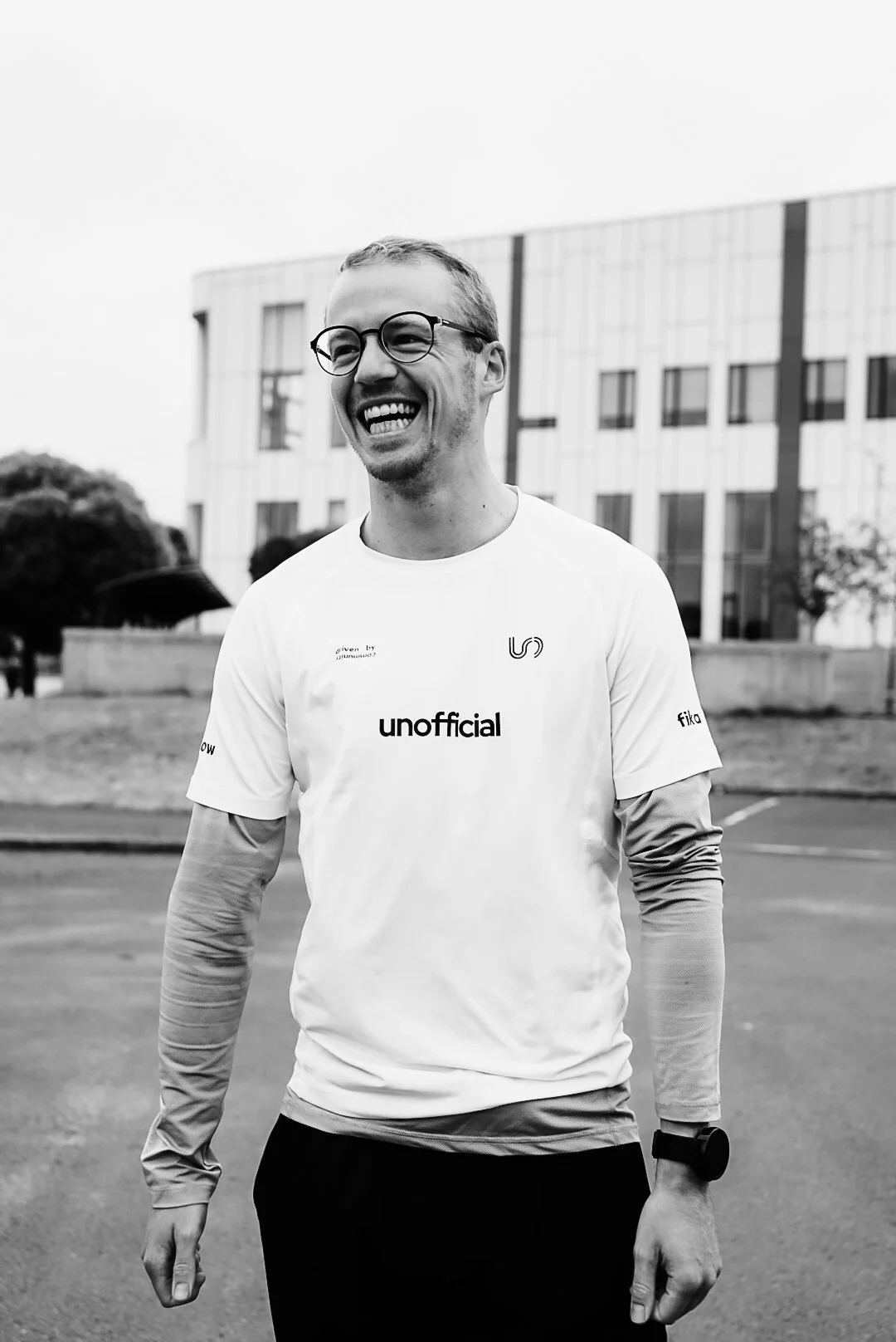 A smiling young man wearing glasses and a sports t-shirt standing outdoors on a city street.