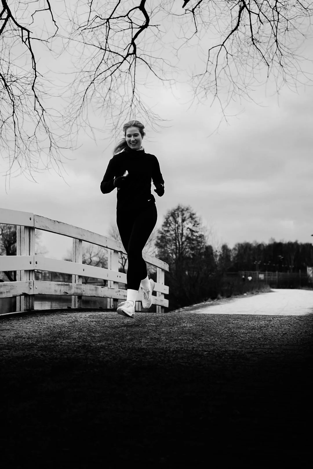 A woman jogging outdoors on a path during cloudy weather, surrounded by leafless trees.