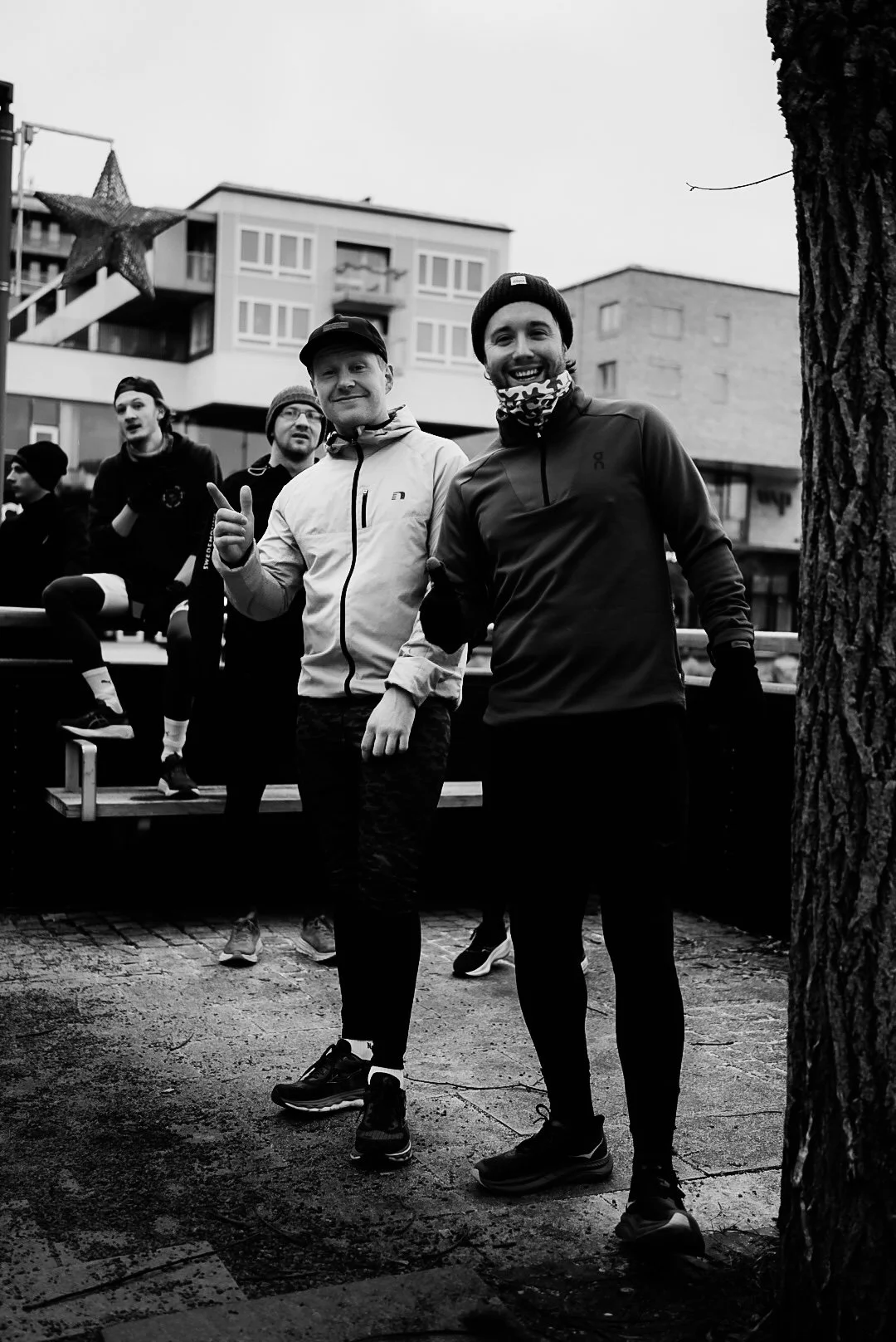 Group of men outdoors in winter clothing, smiling and posing for a photo, with a building and a star decoration in the background.