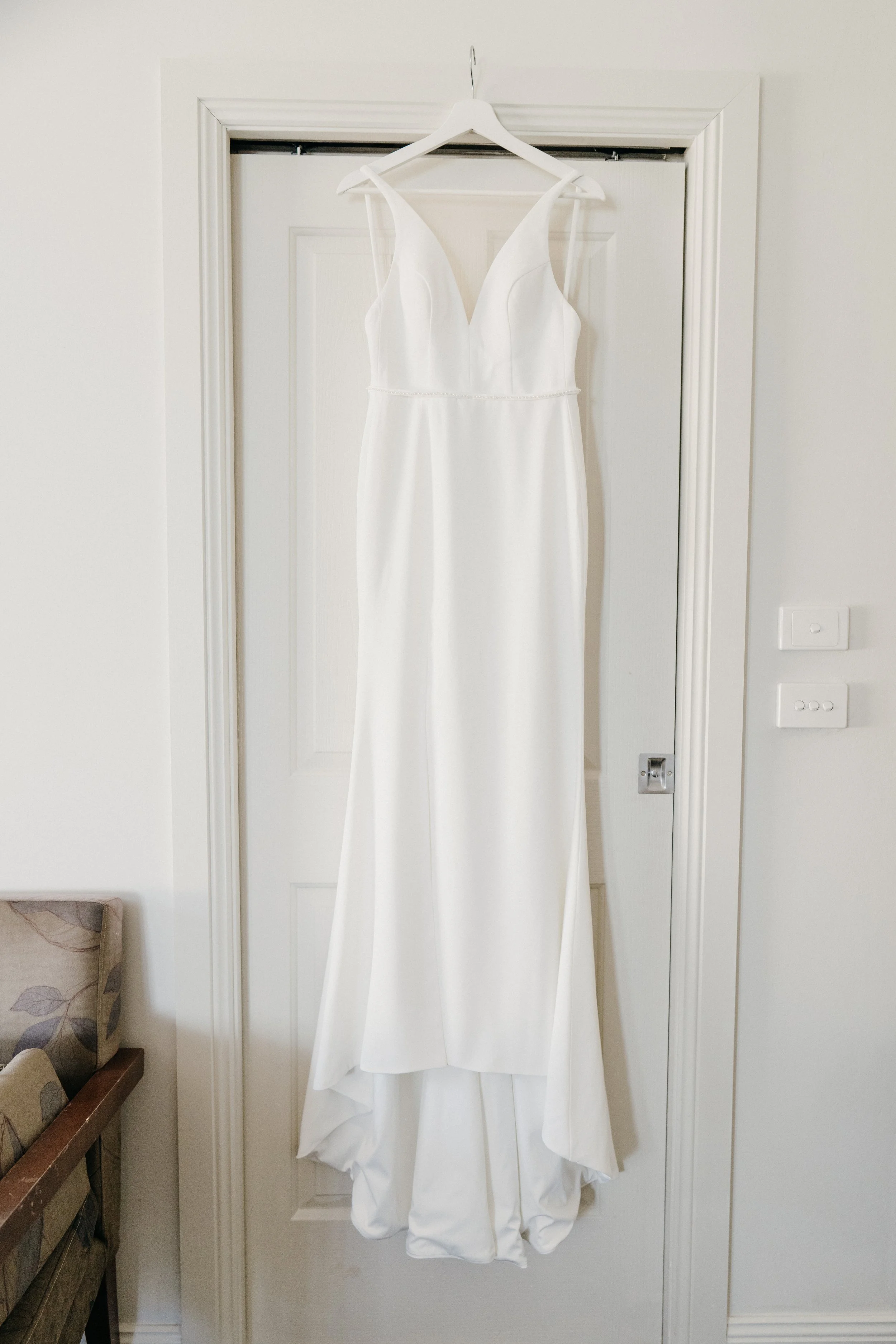 White wedding dress hanging on a white hanger on a door.