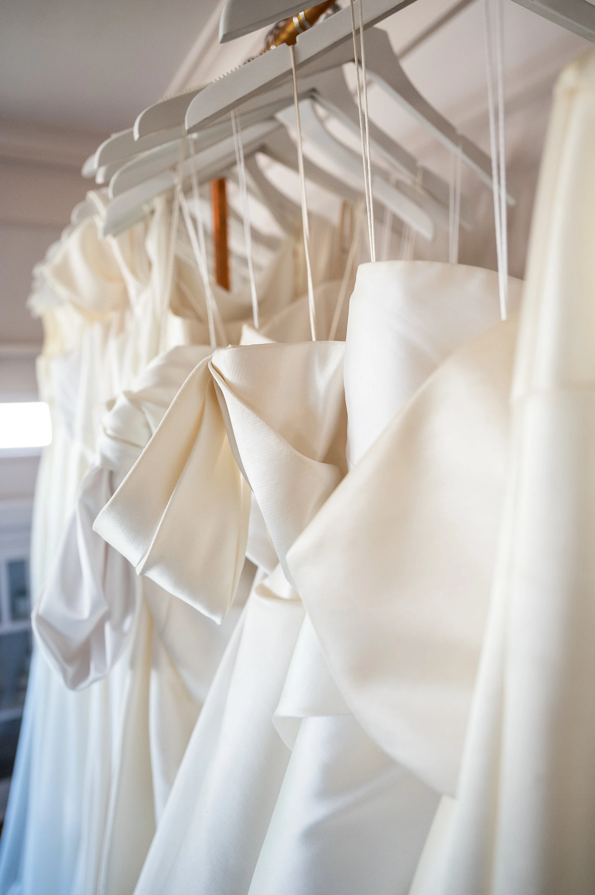 Multiple ivory or white wedding dresses hanging on white hangers on a clothing rack.