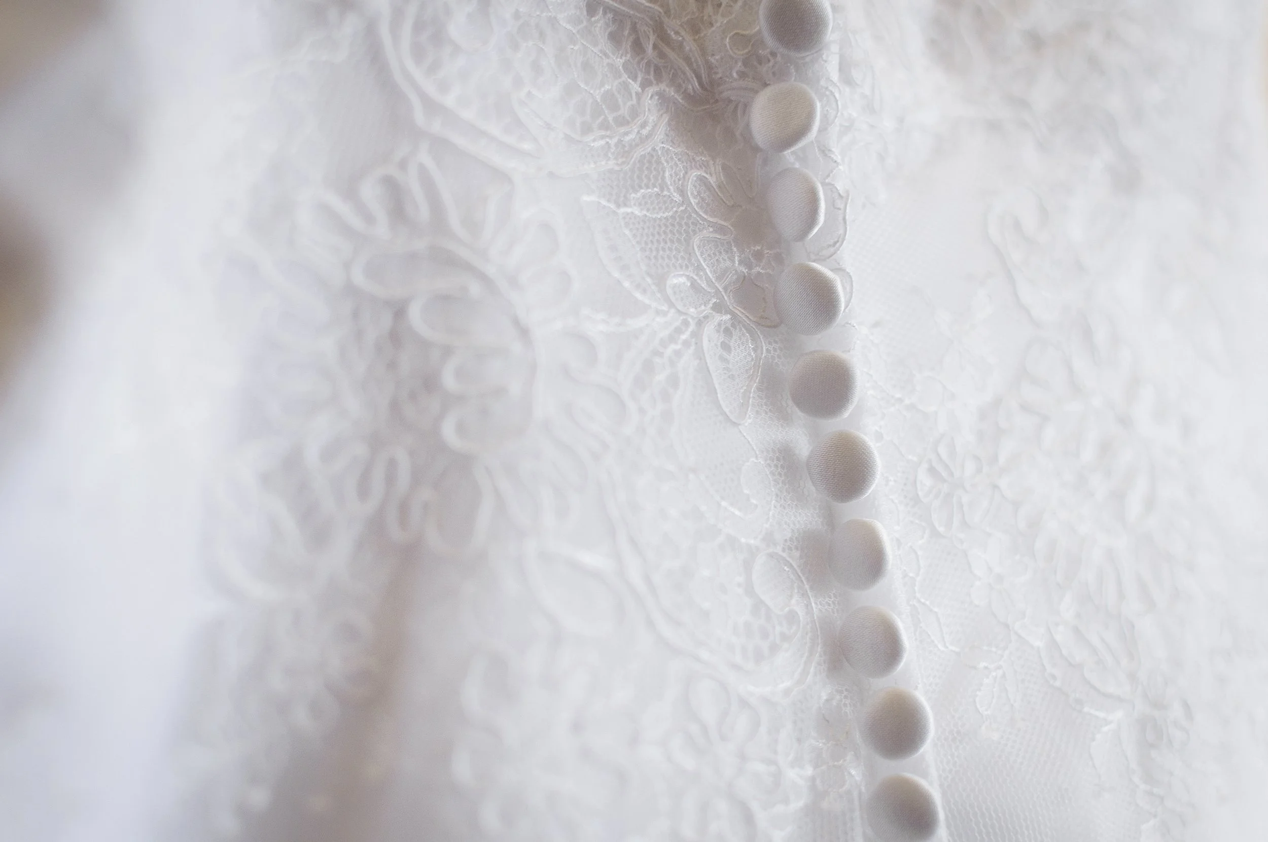 Close-up of white lace fabric with a row of fabric-covered buttons.