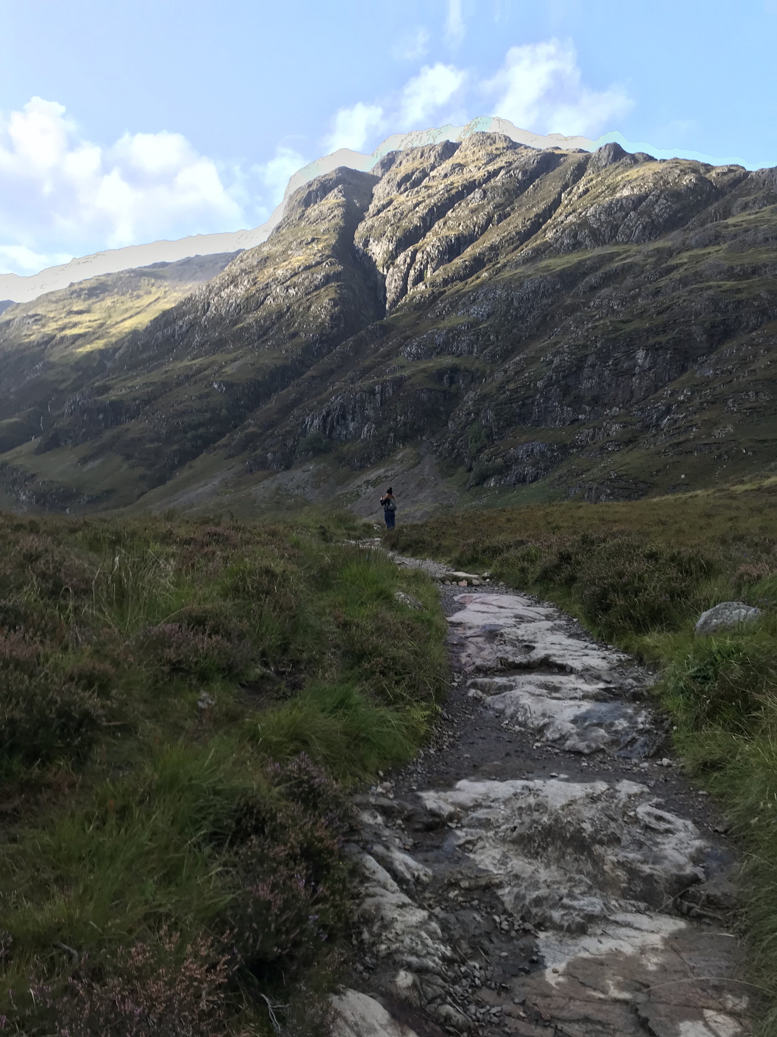 Woman walking on a trail to the base of a mountain.