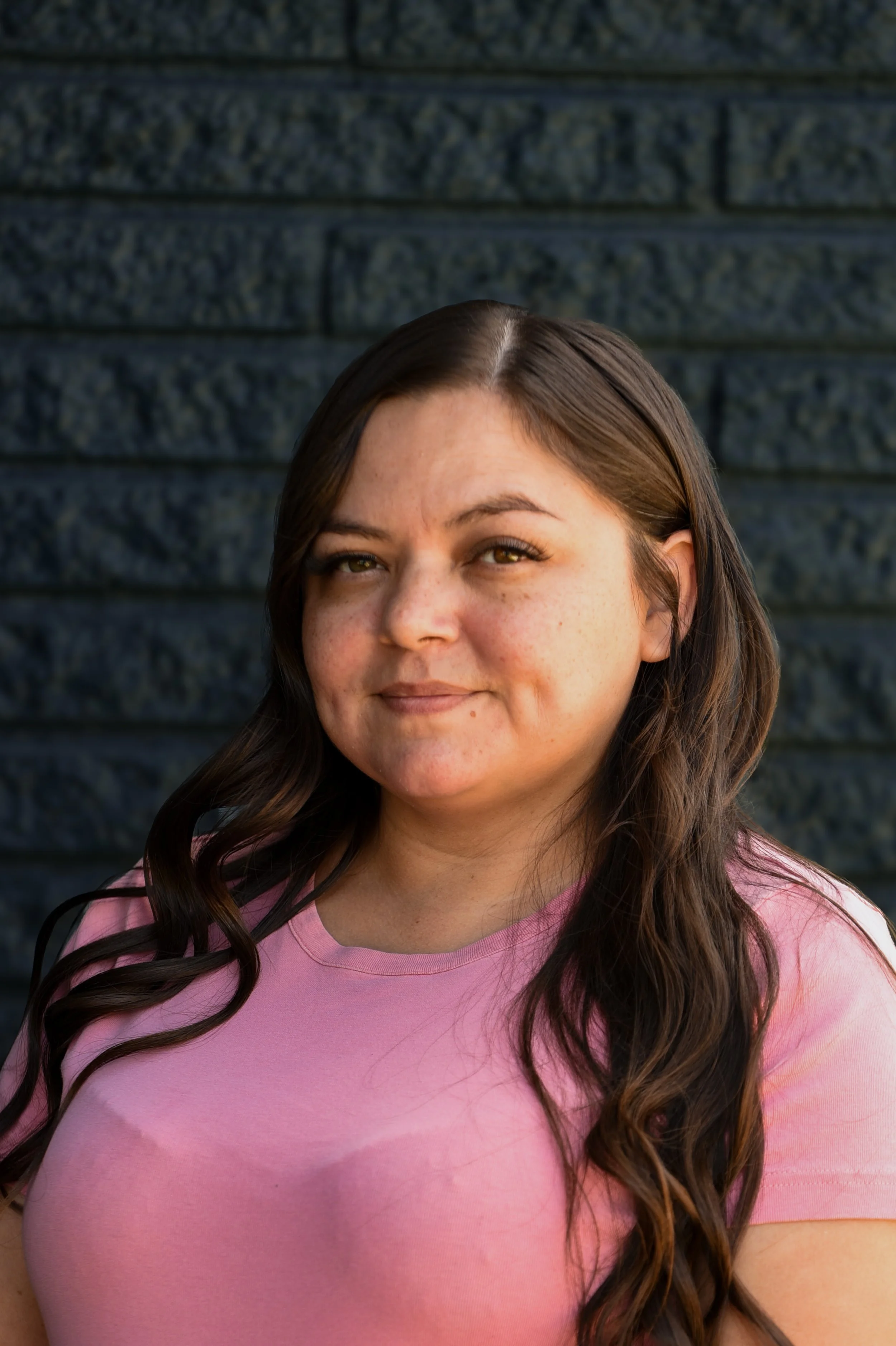 Portrait of a smiling woman with long brown hair wearing a black top against a black background.
