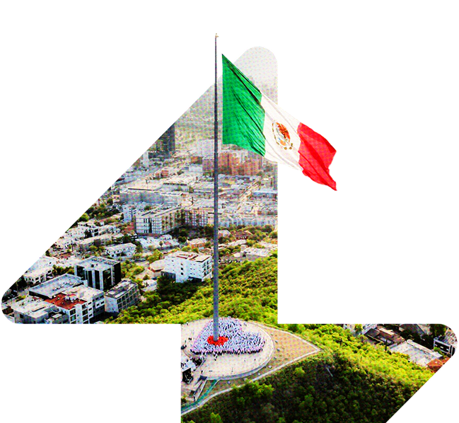 Bandera de México ondeando en un mástil en un parque con edificios y árboles alrededor.