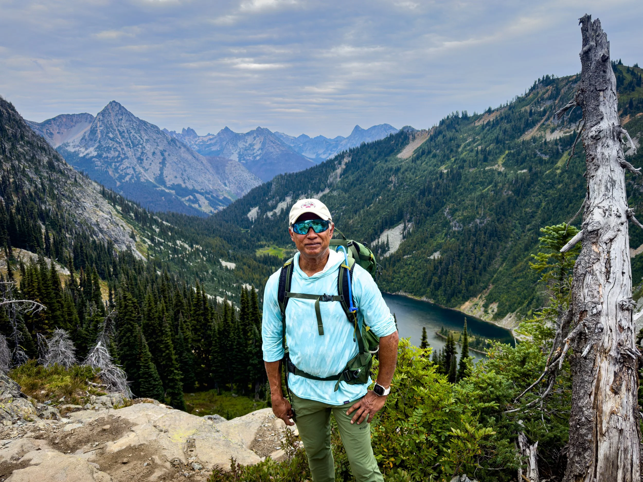 Sundar wearing hiking gear above a mountain lake and forested valley.