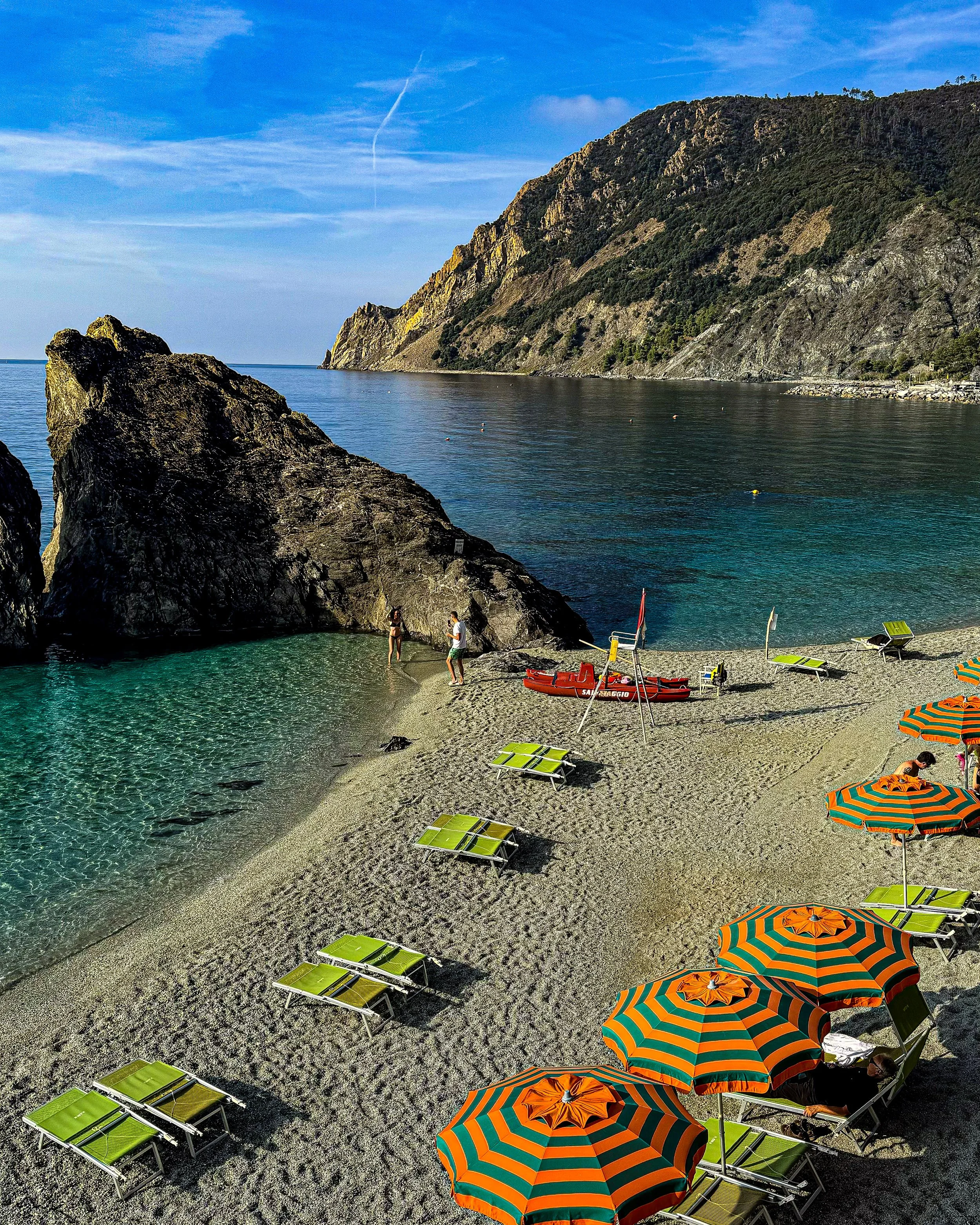 A sheltered rocky cove with clear water, kayaks and striped beach umbrellas.
