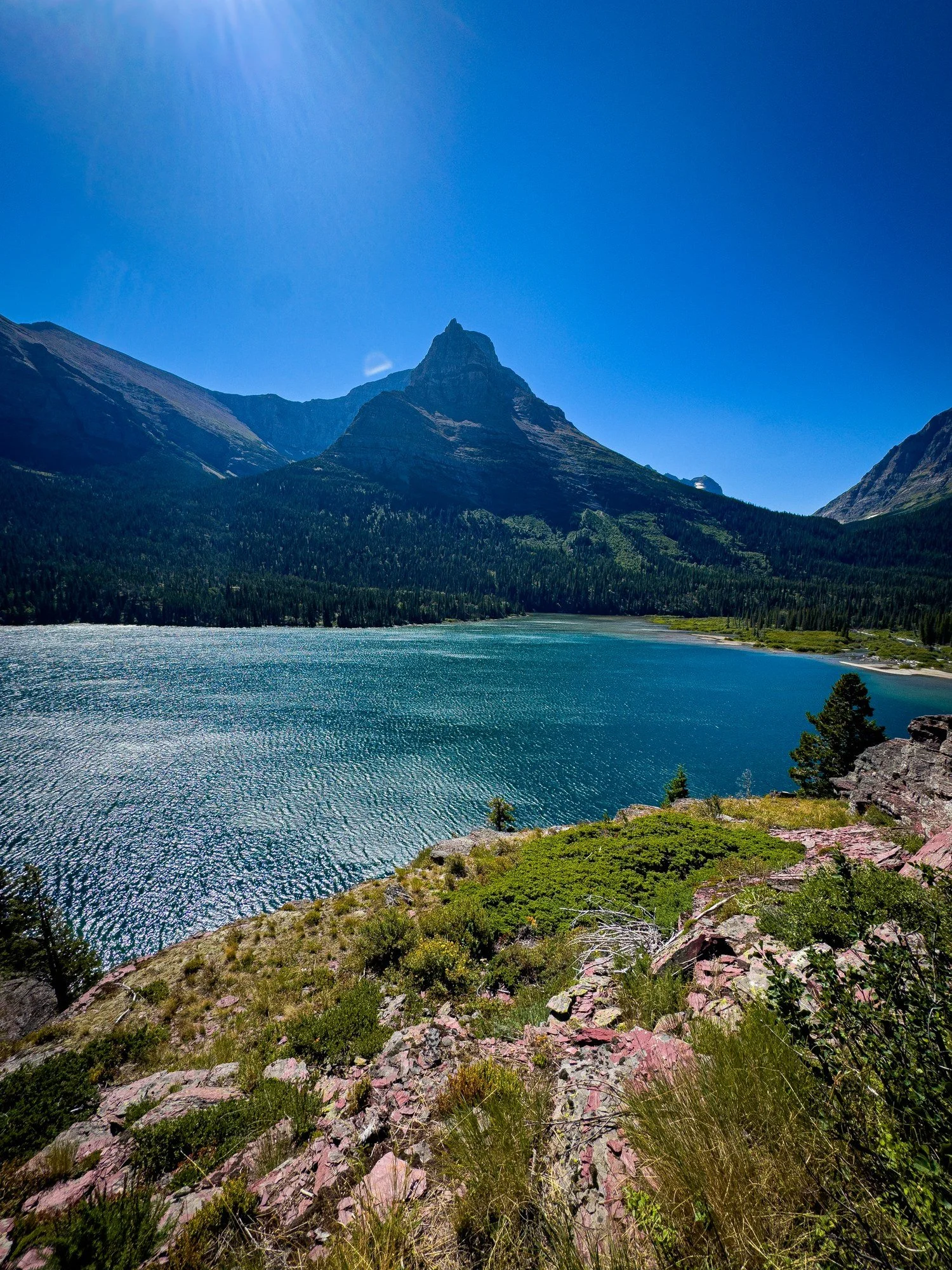 A brilliant blue lake beneath jagged mountain peaks, with evergreen forest along the shore.