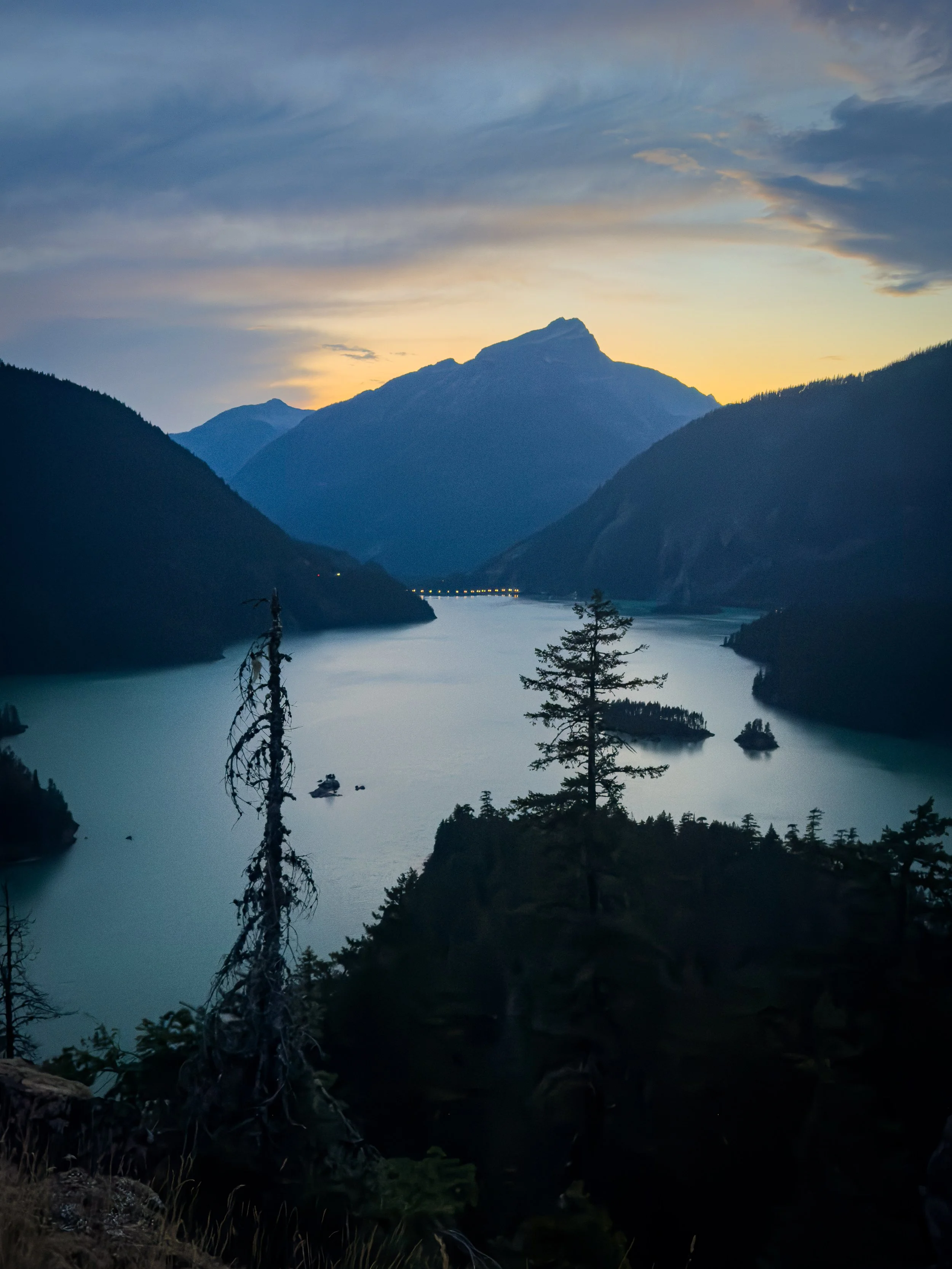 A mountain lake and wooded islands beneath silhouetted peaks and a warm dusk sky.