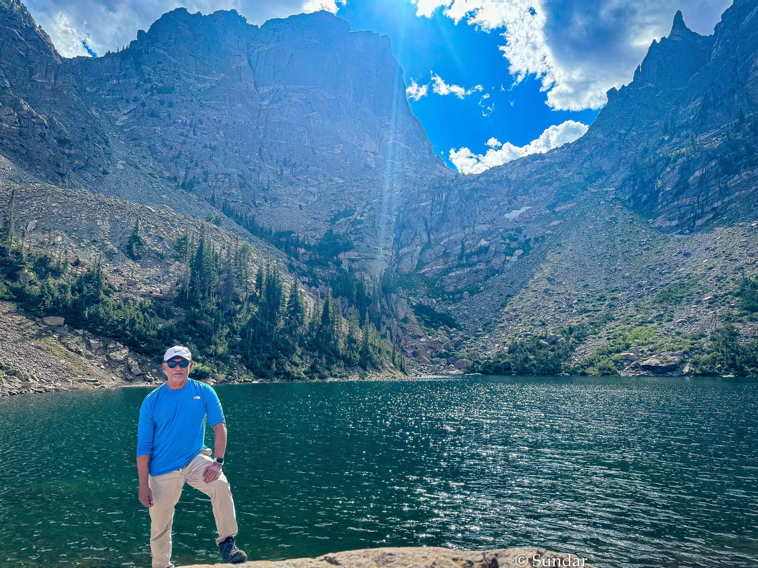 Sundar beside a mountain lake during an active travel journey.