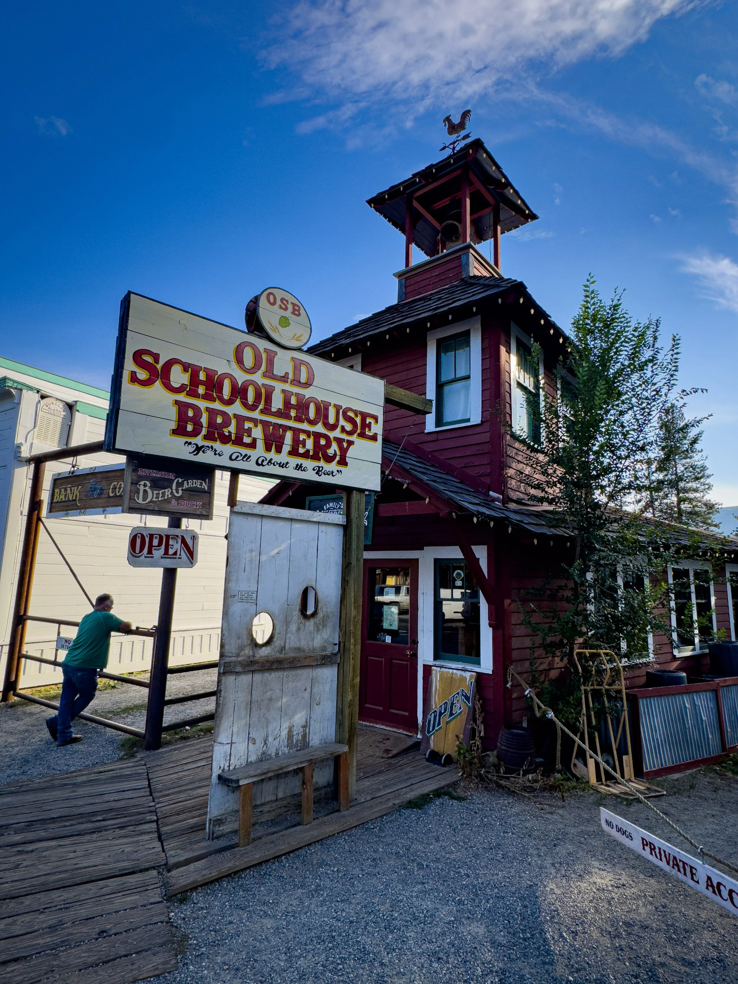 Old Schoolhouse Brewery’s sign and red building beside a wooden entrance walkway.