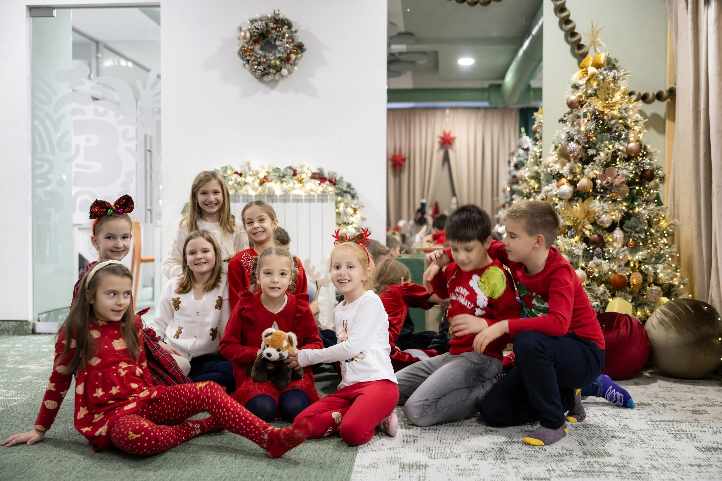 Group of children in Christmas pajamas and sweaters gathered in a festive room with Christmas trees, ornaments, and holiday decorations smiling and posing for a photo.