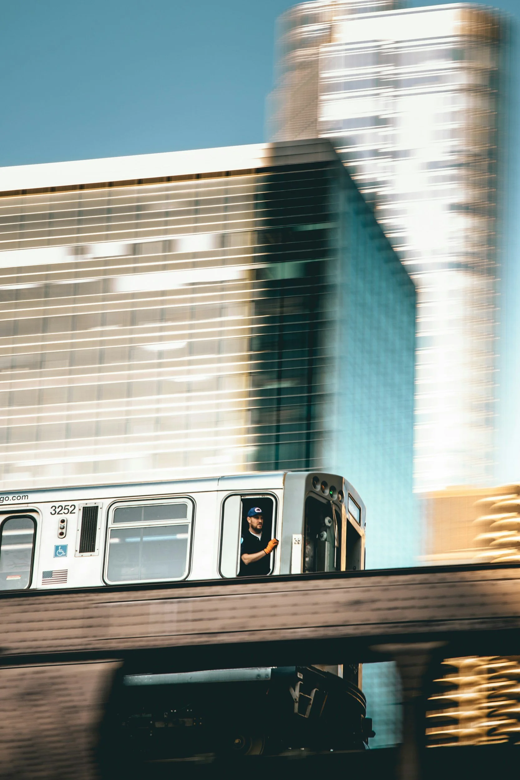 A moving train with a man standing in the open door, against a backdrop of tall skyscrapers in a cityscape.