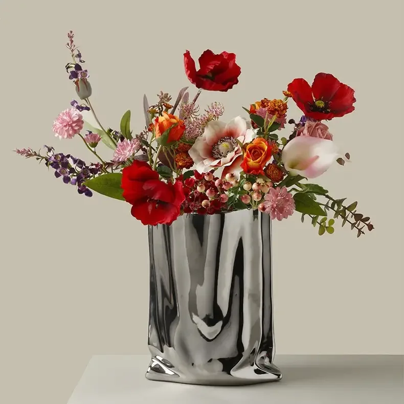 A floral arrangement in a reflective silver vase with pink, red, orange, purple, and white flowers.