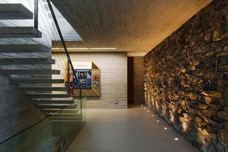 acesso aos dormitórios:
Um grupo de pequenos pontos embutidos no piso dá destaque à parede de pedra.
Ao fundo, uma estreita luminária linear wallwasher ilumina a parede e a obra de arte.