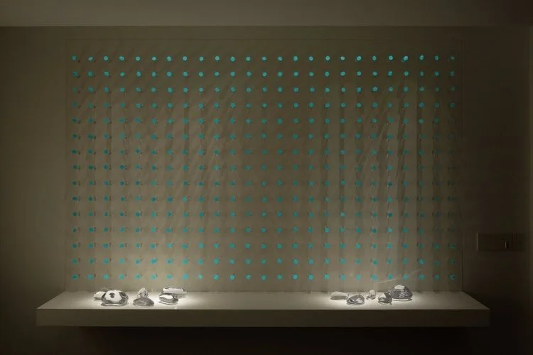 luz ou cor?
De início parecem apenas objetos pintados de uma cor opaca, espécie de batons arranjados sobre um painel vertical.
Nem parece que aquelas cores, um vermelho terroso, um azul cinzento, são, na verdade, luz. Apenas quando o ambiente se