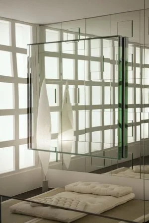 refractal
Poderíamos estar num quarto japonês — e estamos: um tatame, delicadas luminárias de papel microplissado, e uma divisória que quase se faz passar por aquelas de papel arroz emolduradas em quadriculado. Atrás da divisória, a luz difusa, eté