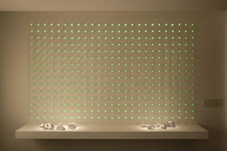 luz ou cor?
De início parecem apenas objetos pintados de uma cor opaca, espécie de batons arranjados sobre um painel vertical.
Nem parece que aquelas cores, um vermelho terroso, um azul cinzento, são, na verdade, luz. Apenas quando o ambiente se