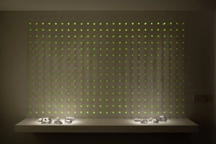 luz ou cor?
De início parecem apenas objetos pintados de uma cor opaca, espécie de batons arranjados sobre um painel vertical.
Nem parece que aquelas cores, um vermelho terroso, um azul cinzento, são, na verdade, luz. Apenas quando o ambiente se