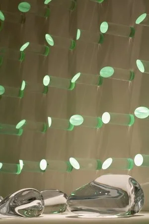 luz ou cor?
De início parecem apenas objetos pintados de uma cor opaca, espécie de batons arranjados sobre um painel vertical.
Nem parece que aquelas cores, um vermelho terroso, um azul cinzento, são, na verdade, luz. Apenas quando o ambiente se