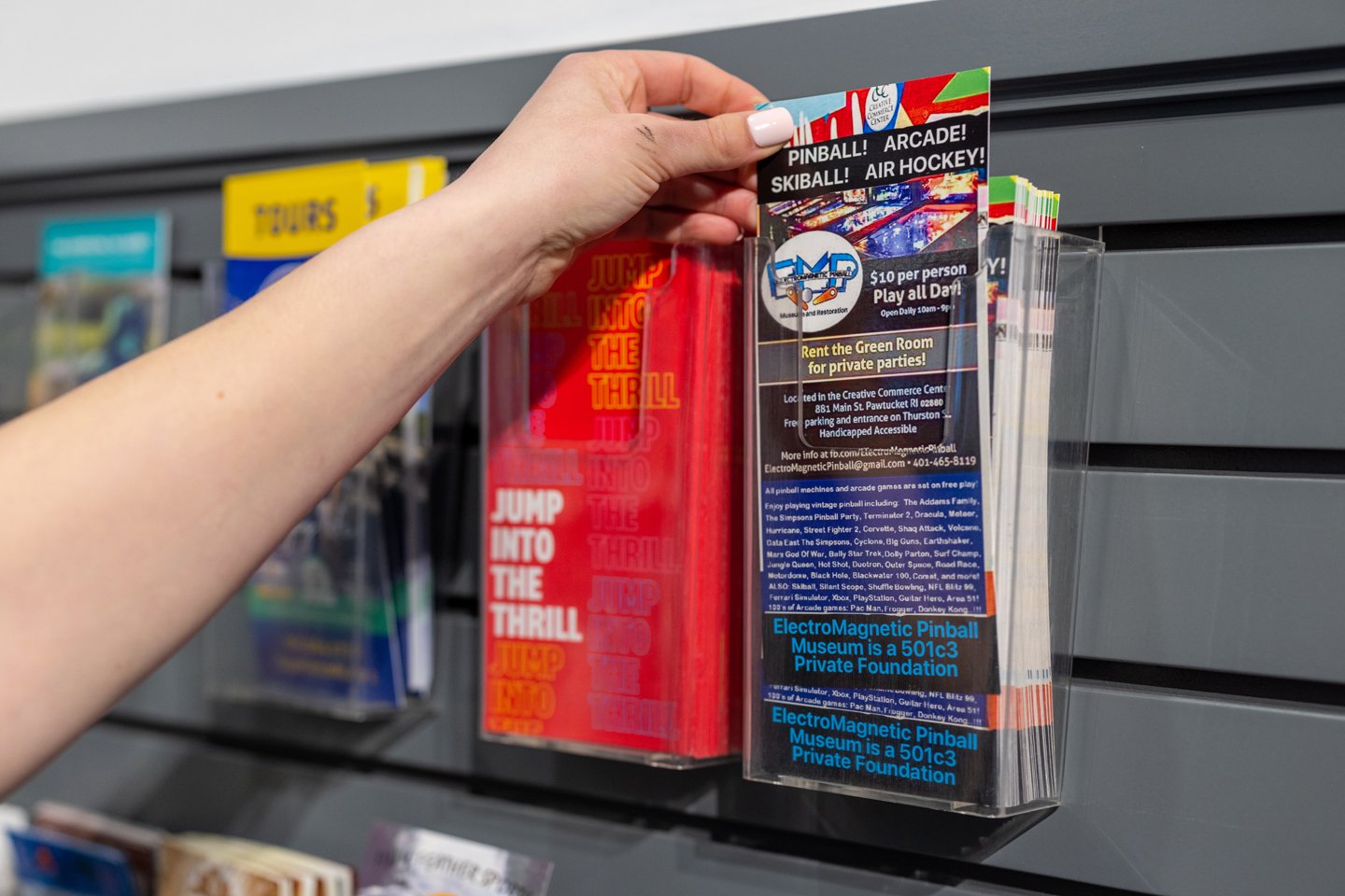 Person holding a brochure for a pinball and arcade museum from a display rack.