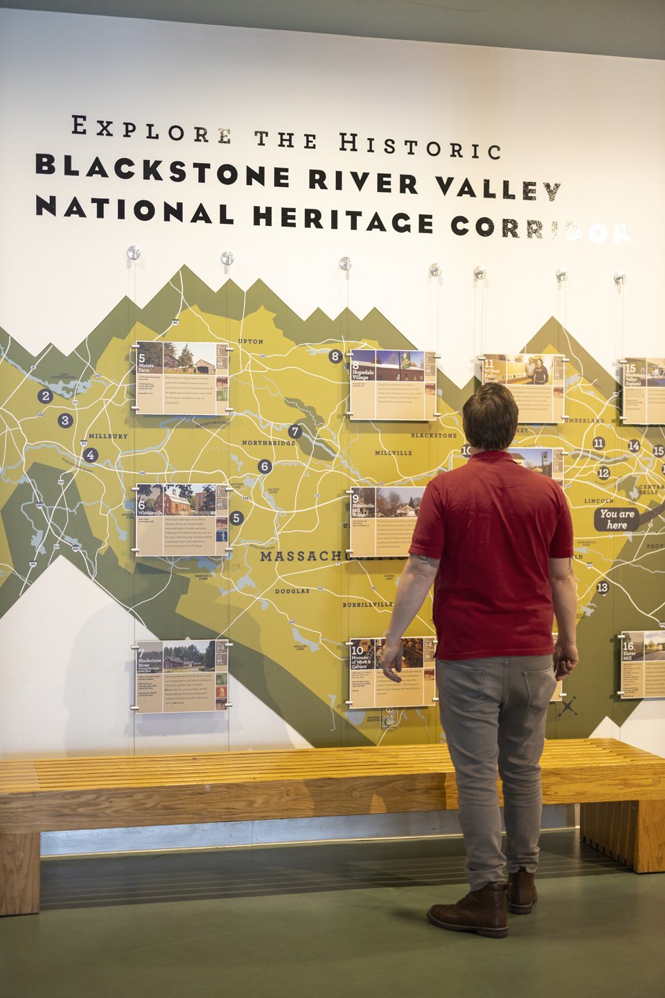 Man examining a wall map display of the Blackstone River Valley National Heritage Corridor with informational panels and locations marked, Massachusetts.