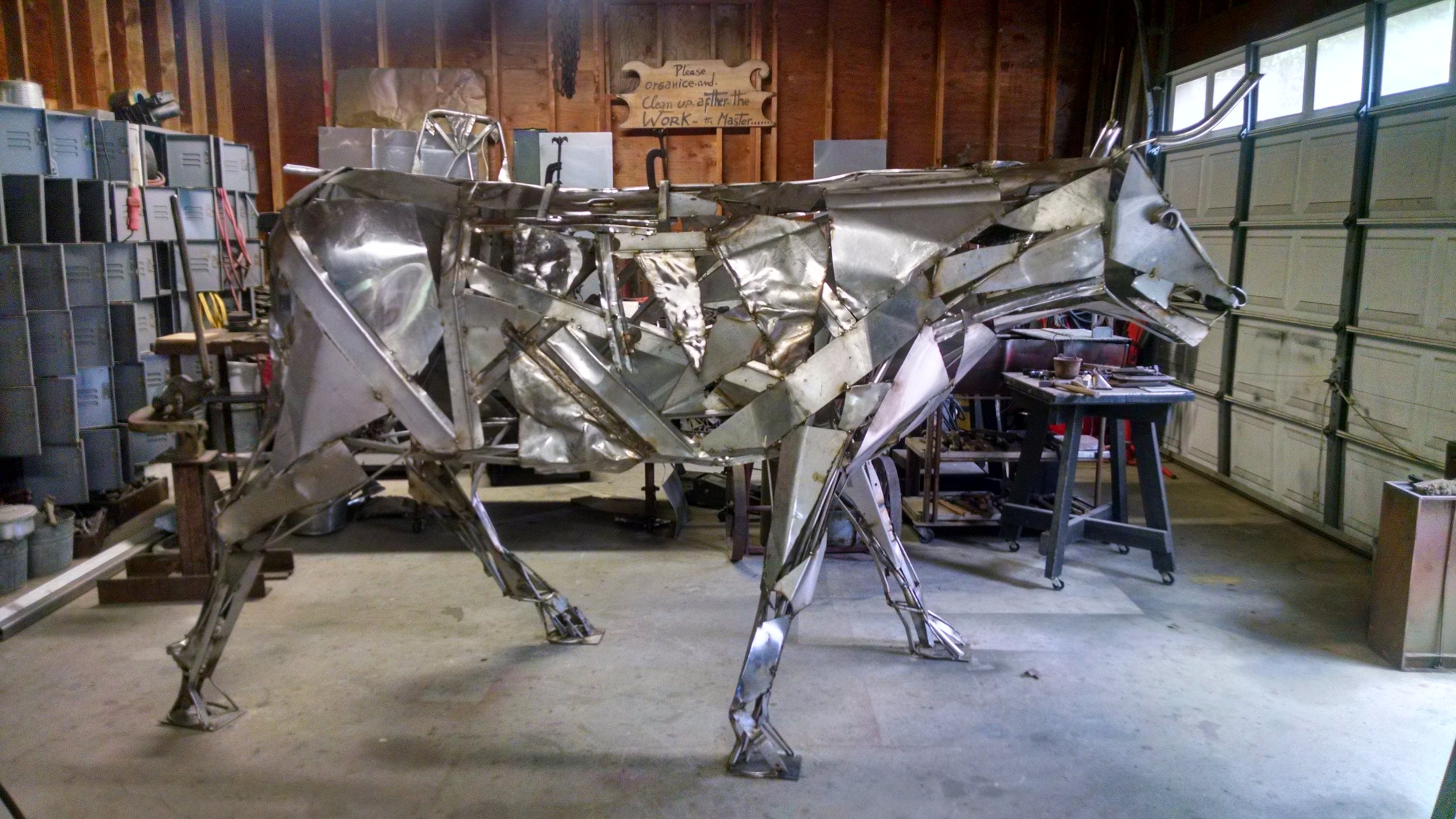 Large metal bull sculpture in workshop with tools and equipment in the background.