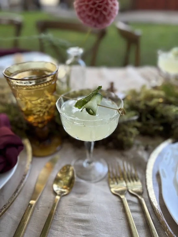 Two craft cocktails on a beautifully set table with gold silverware and greenery.