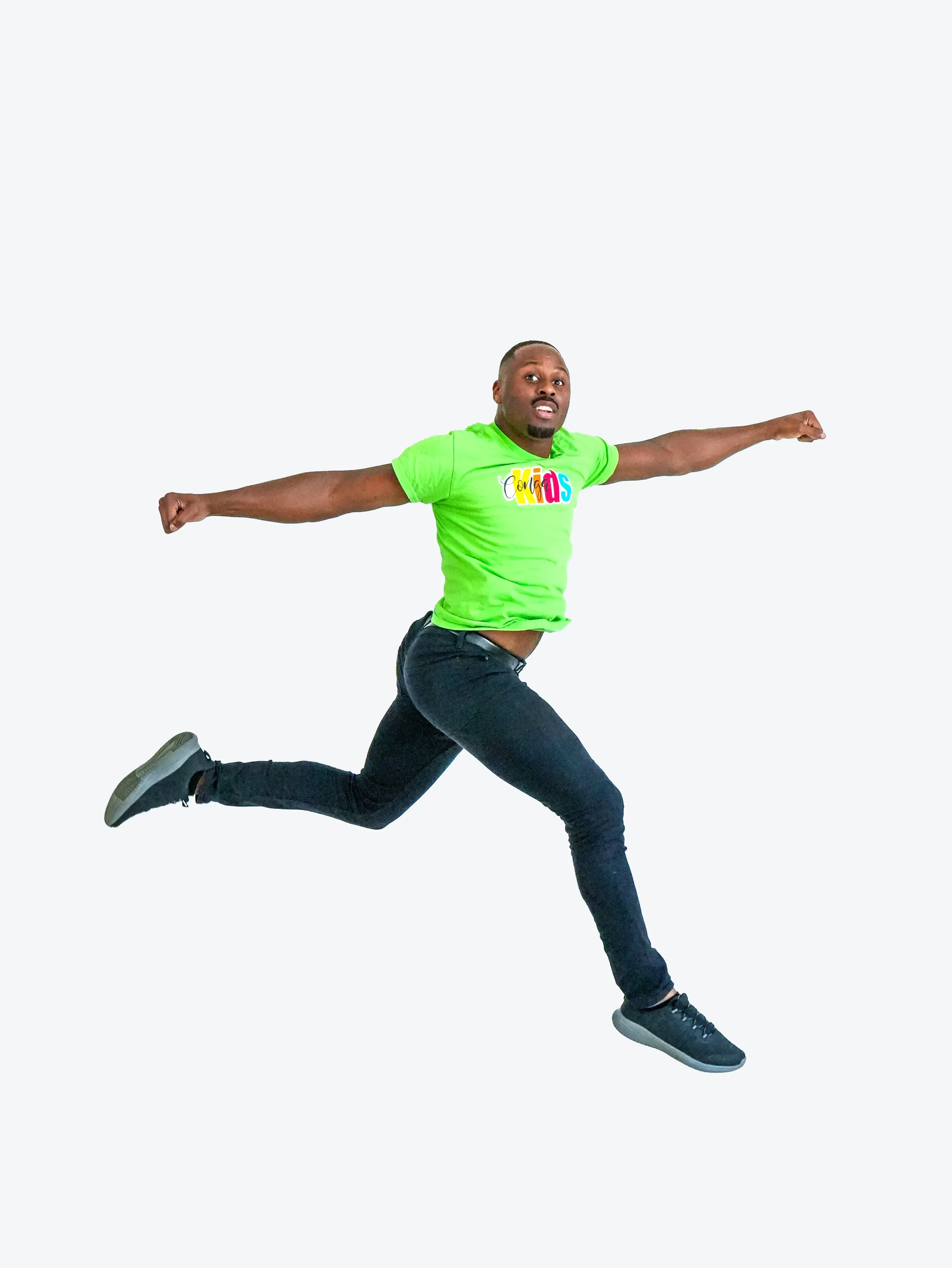 A man mid-jump with arms outstretched, wearing a green t-shirt and black pants, against a plain light background.