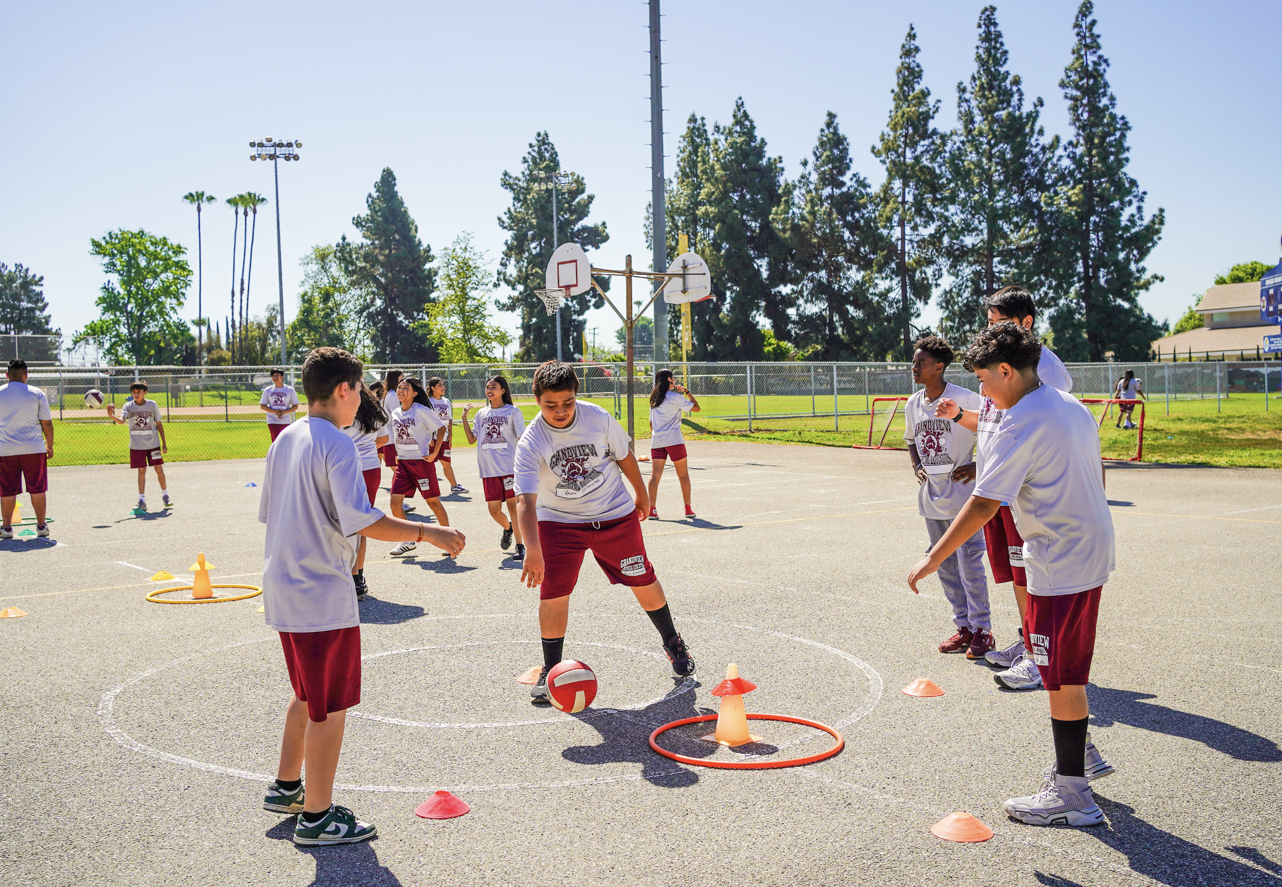 Group of children on outdoor basketball court playing with volleyball and cones