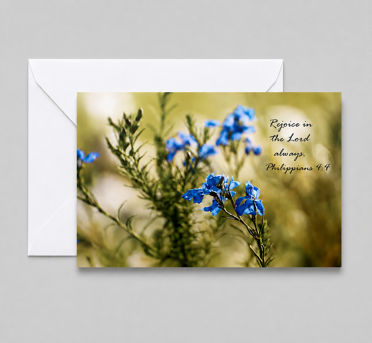 Greeting card with a photo of blue flowers and a biblical quote from Philippians 4:4 that says, 'Rejoice in the Lord always.'