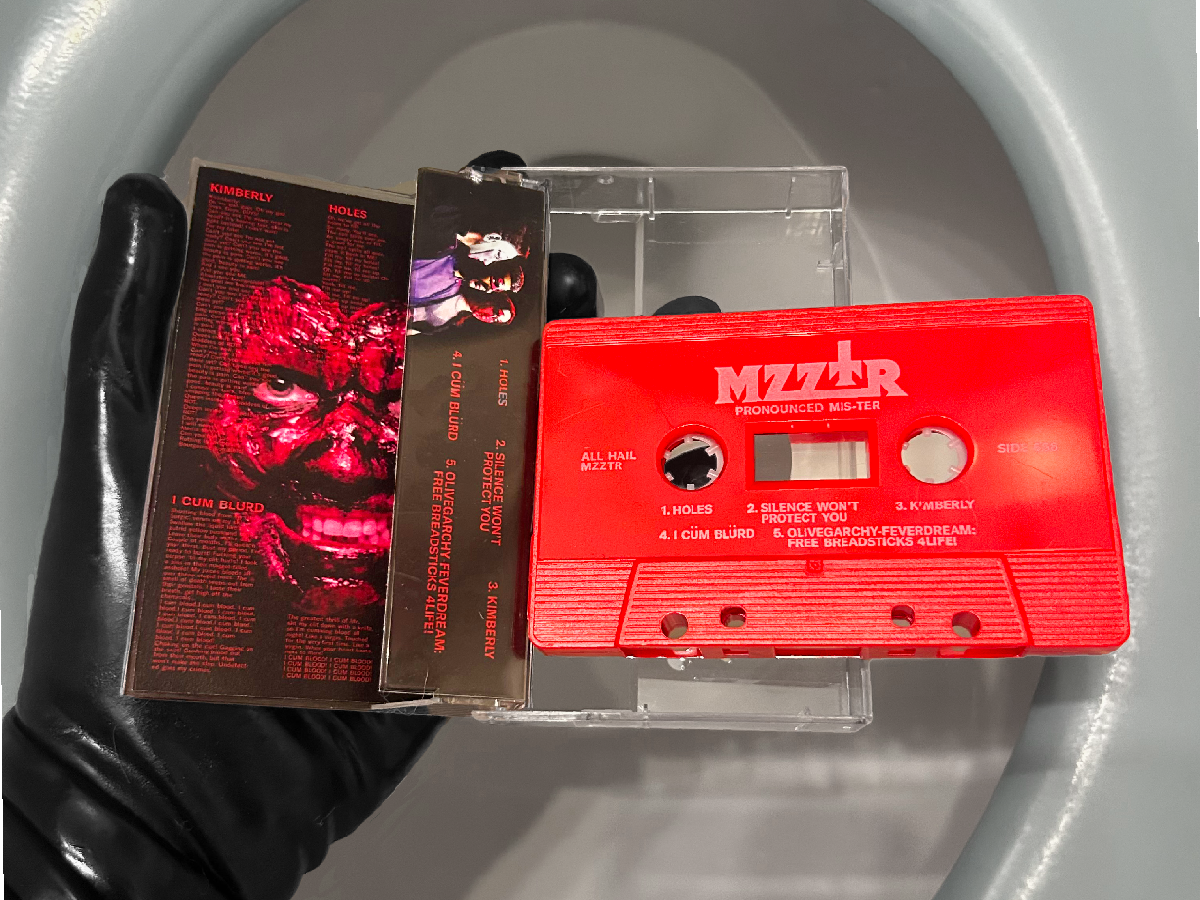 A red cassette tape labeled 'MZZTR' with song titles and track information, held in a gloved hand over a curved white surface. Latex MZZTR holds their debut EP Prnounced: MIS-TER Pre Order Now!