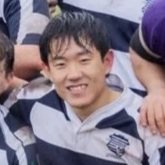 A young person smiling outdoors, wearing a striped sports jersey.