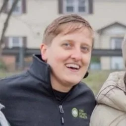 An athlete in a blue and yellow sports uniform with a helmet, standing on an indoor sports court with red and yellow poles in the background.