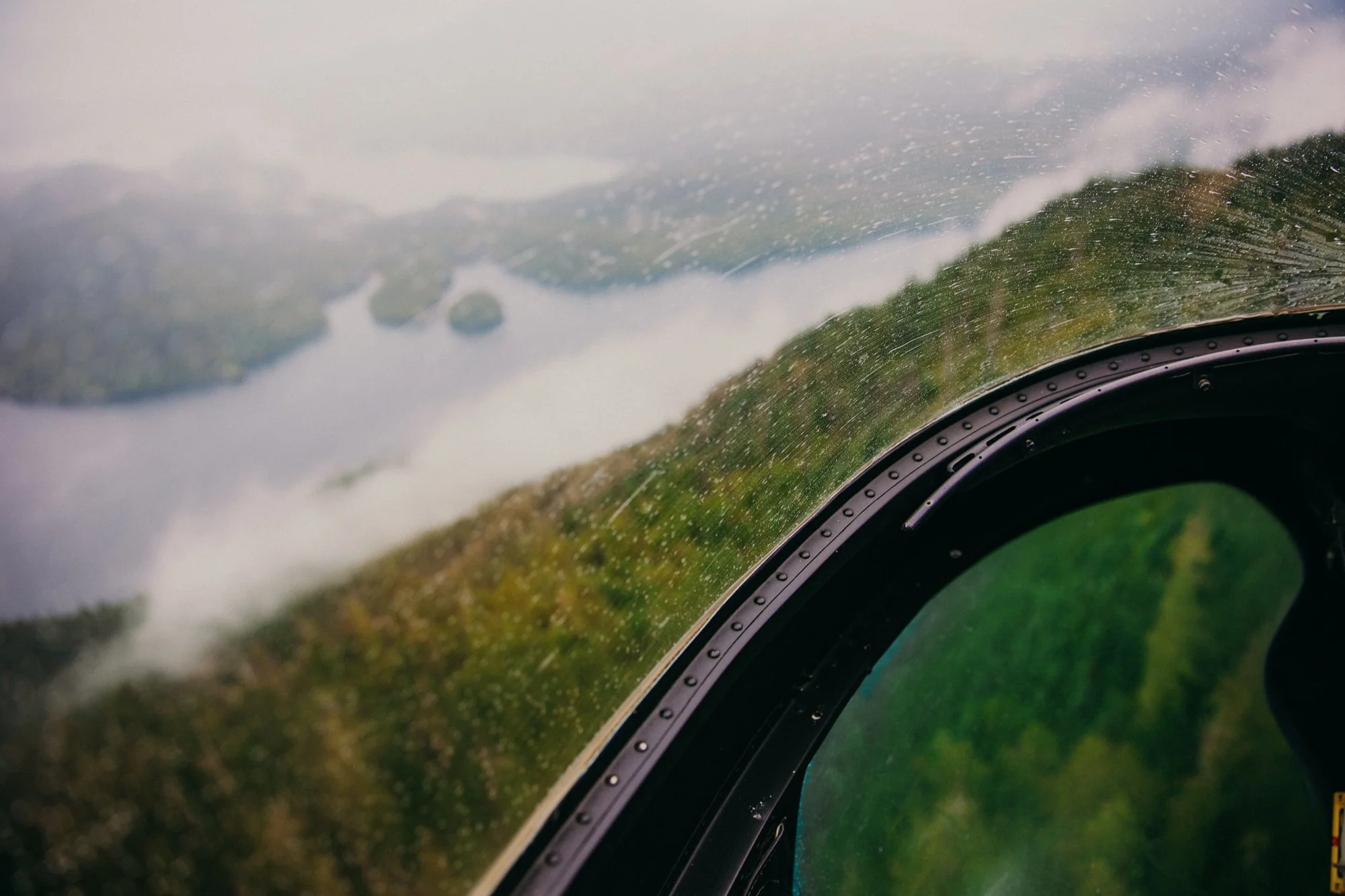 Aerial view of a river and lush green landscape viewed from an aircraft cockpit with rain on the window.
