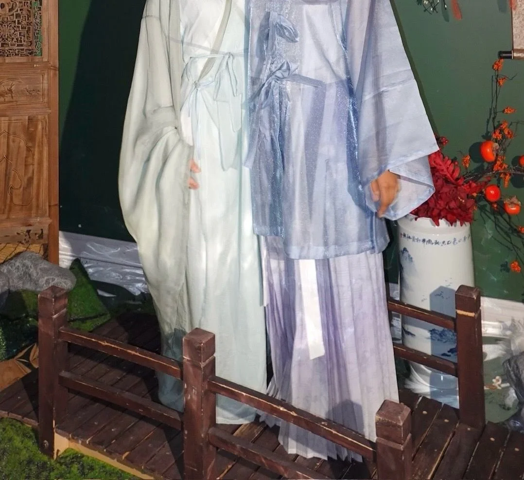 Display of traditional Japanese clothing on mannequins, including kimonos in pastel colors, set in a room with decorative plants and furniture.