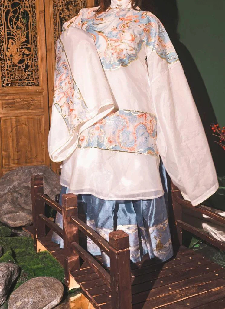 A traditional Asian garment featuring pastel-colored swirling cloud-like patterns, displayed on a mannequin inside a wooden structure with rocks and greenery around.