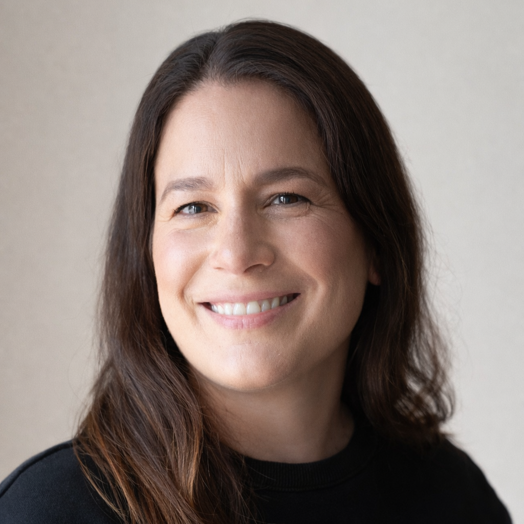 Close-up of a woman with long brown hair smiling, wearing a black top, against a neutral background.