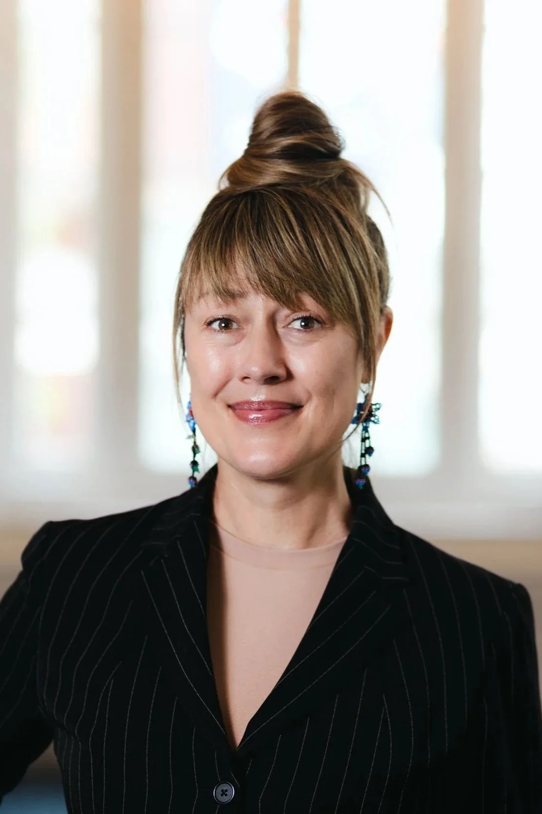 A woman with long black hair, smiling, wearing a black top, against a gray gradient background.
