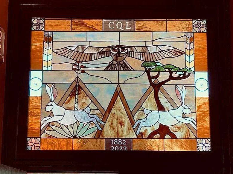 stained glass window in a neutral palette with two rabbits, and owl, mountains and agave