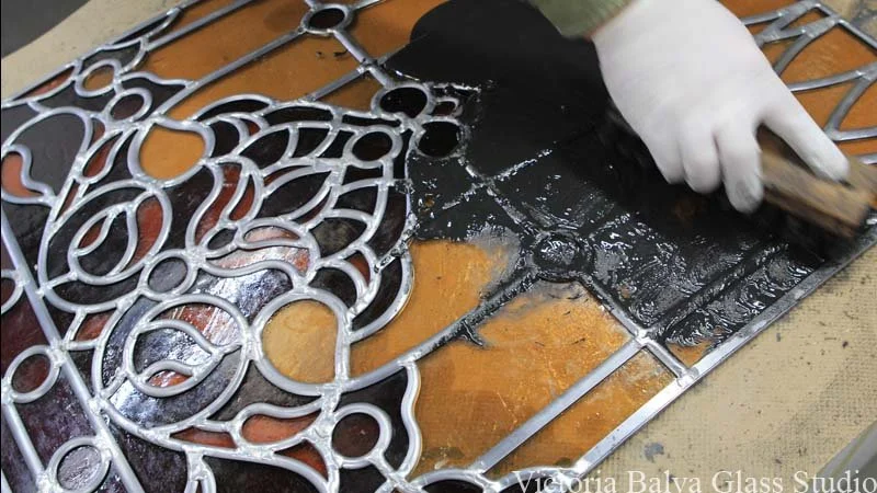 person applying stained glass cement to a lead came panel