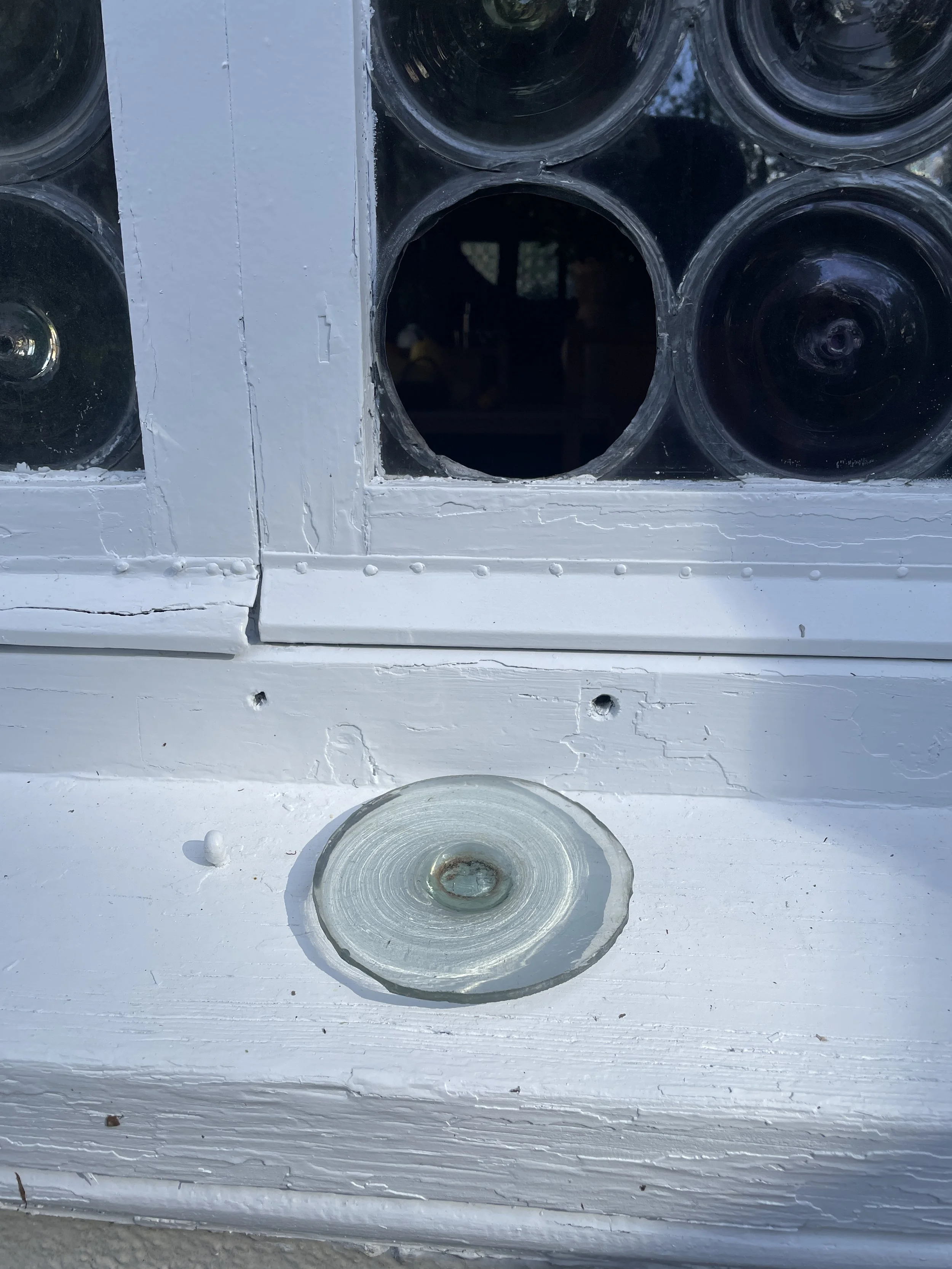 Close-up of a white-painted wood framed window with leaded glass rondel popped out and ready for repair